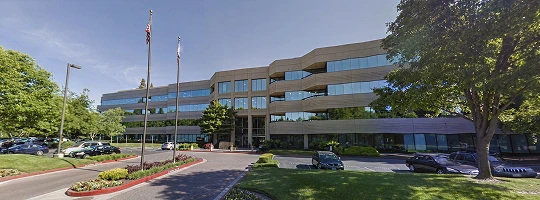 A large multi-story office building in Sacramento with reflective windows, flags at the entrance, and a landscaped driveway.