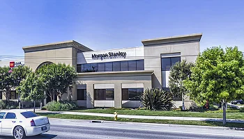 Street view of a two-story office building in Salinas with a "Morgan Stanley" sign, trees, and parked cars in front.