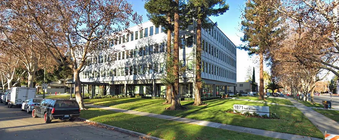 Exterior view of a modern four-story office building in San Jose, surrounded by trees and parked cars along the street.