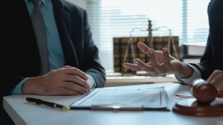 Two professionals in suits discussing legal documents at a desk with a gavel and law books.