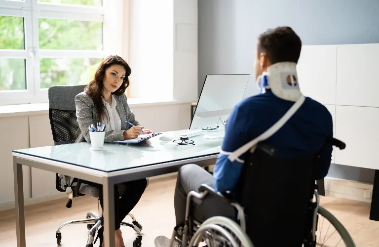 Professional woman in office consulting with man in wheelchair wearing neck brace.