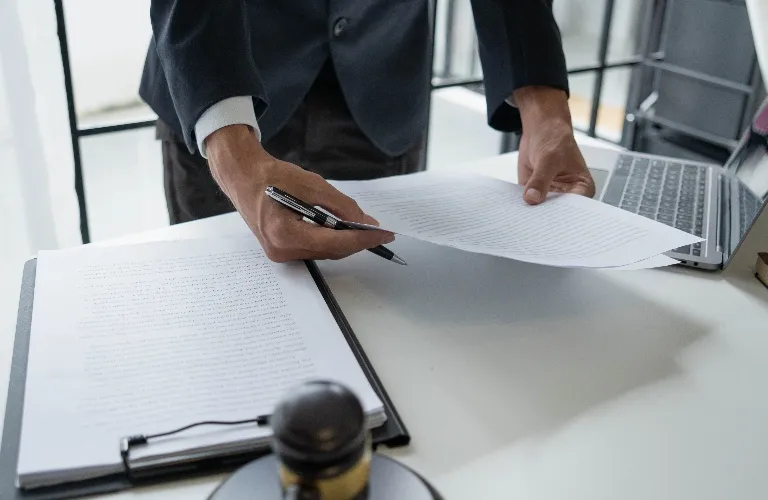 Person in dark suit reviewing documents at white desk with laptop and stamp.