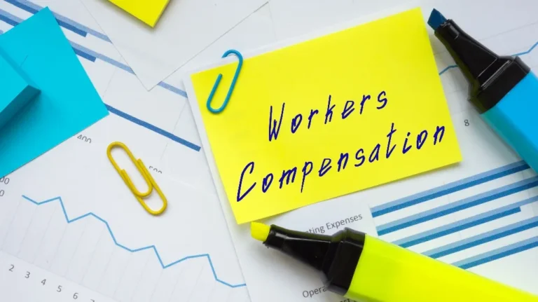 Yellow sticky note with "Workers Compensation" text, blue and yellow paper clips, highlighters, and financial charts.