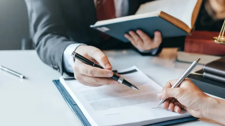 Two individuals in professional attire reviewing and signing a document on a white desk.