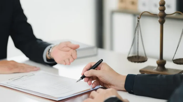 Two professionals in black suits at a desk with legal documents and scales of justice.