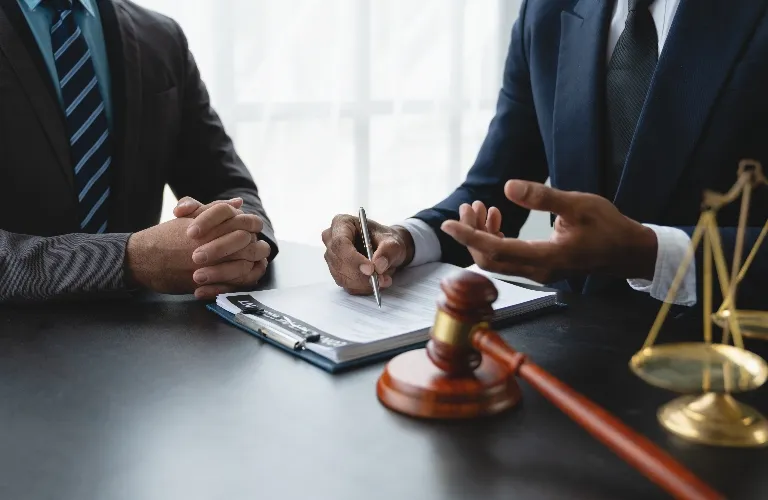 Two men in suits at a desk with legal documents, a gavel, and scales of justice.