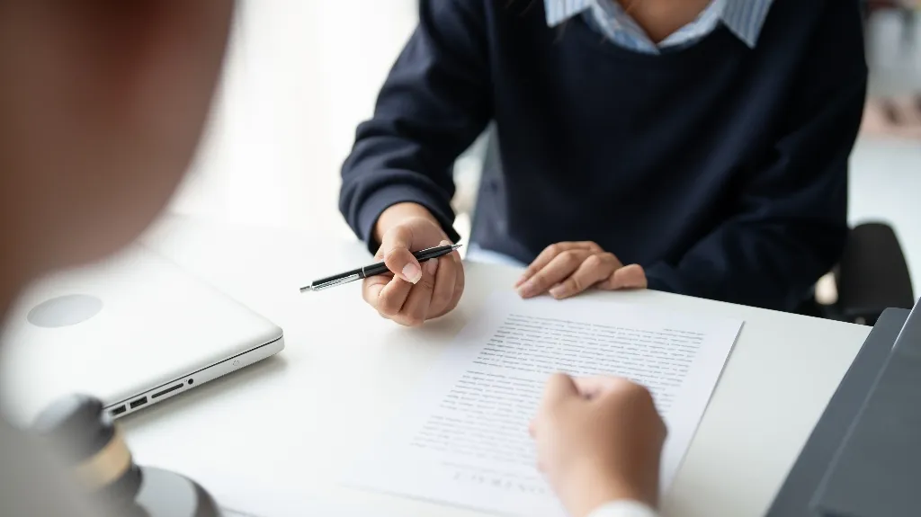 Two individuals engaged in a discussion over a document on a white desk with a laptop nearby.