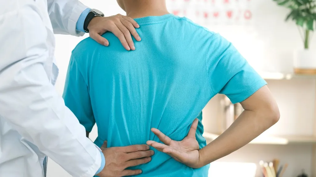 Medical professional examining patient's back with hands, patient wearing blue shirt.