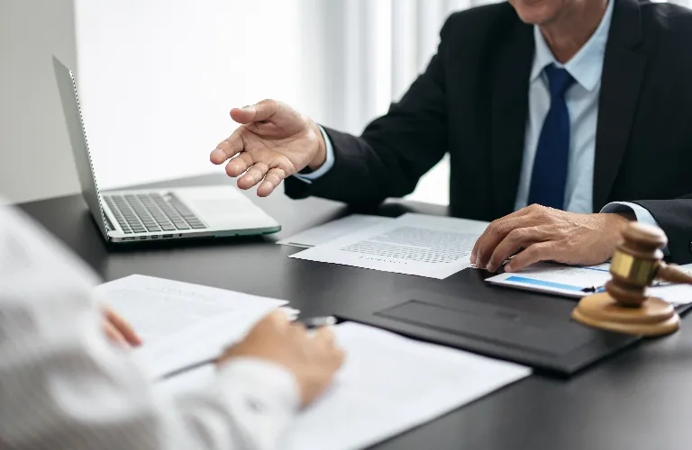 Two professionals in formal attire discussing documents at a desk with a laptop and gavel.