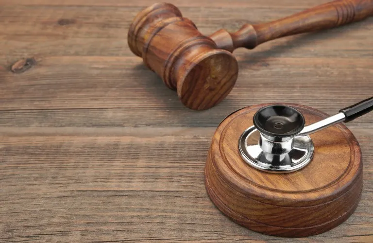 Wooden judge's gavel and sound block with a stethoscope placed on the sound block, on a wooden surface.