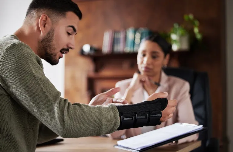 Man with wrist brace explaining to professional woman during consultation in office.
