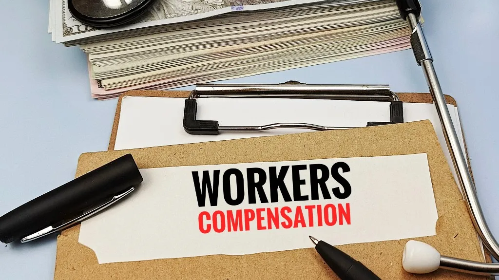 Clipboard with "Workers Compensation" text, pen, stethoscope, and medical documents.