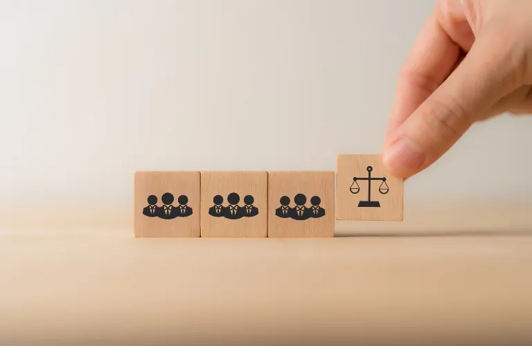 Hand placing wooden block with scale icon next to three blocks with group of business people icons.