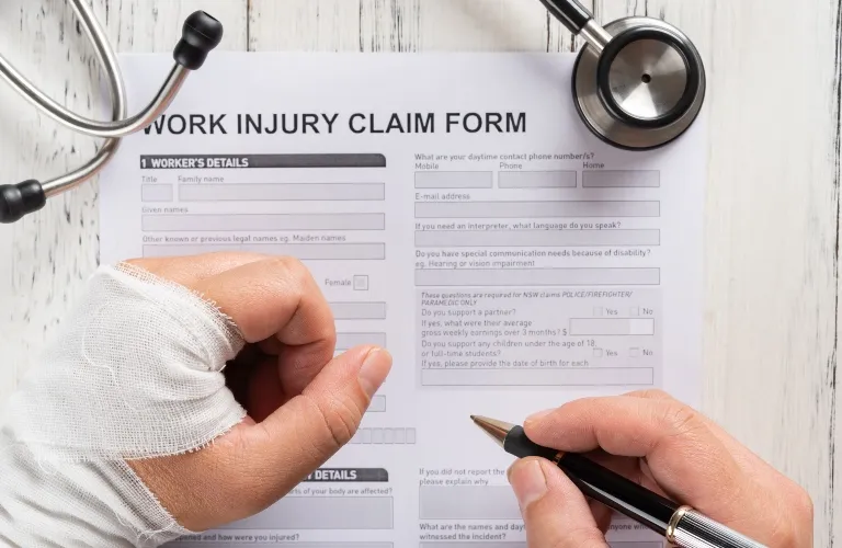 Person with bandaged hand filling out a work injury claim form, stethoscope nearby.