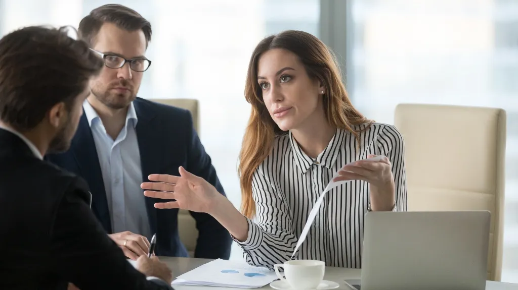 Three professionals engaged in a discussion with documents and a laptop in a modern office.
