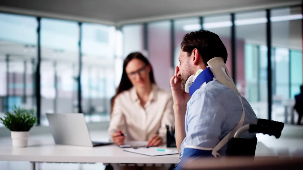 Man with neck brace in wheelchair consulting with female doctor in modern office.