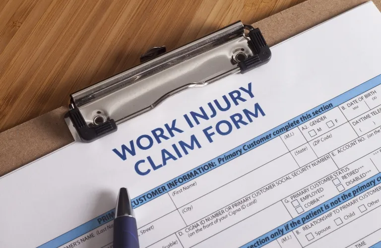 Work injury claim form on clipboard with blue pen on wooden surface.