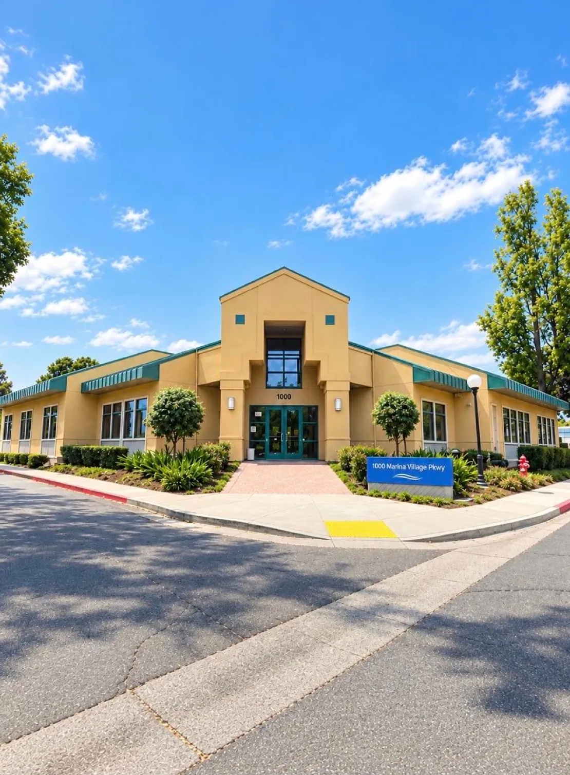 Modern beige commercial building with green trim, large windows, and clear blue sky.