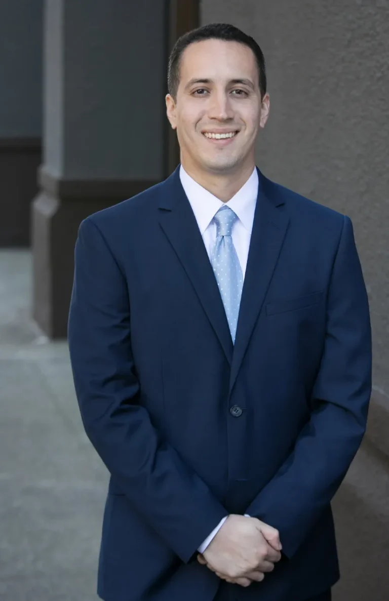 Professional portrait of a smiling man in a navy suit and light blue tie.