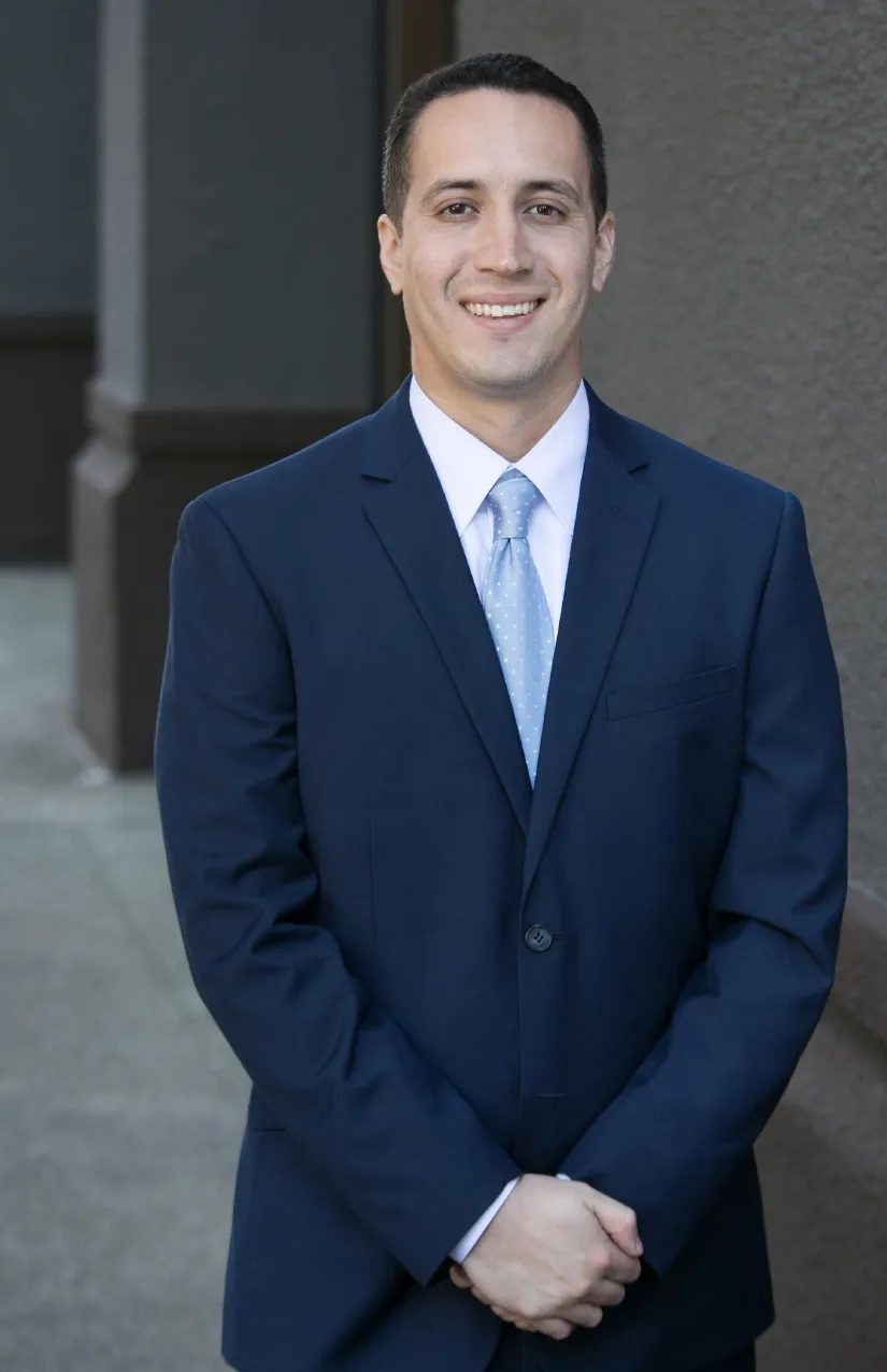 Professional portrait of a smiling man in a navy suit and light blue tie.