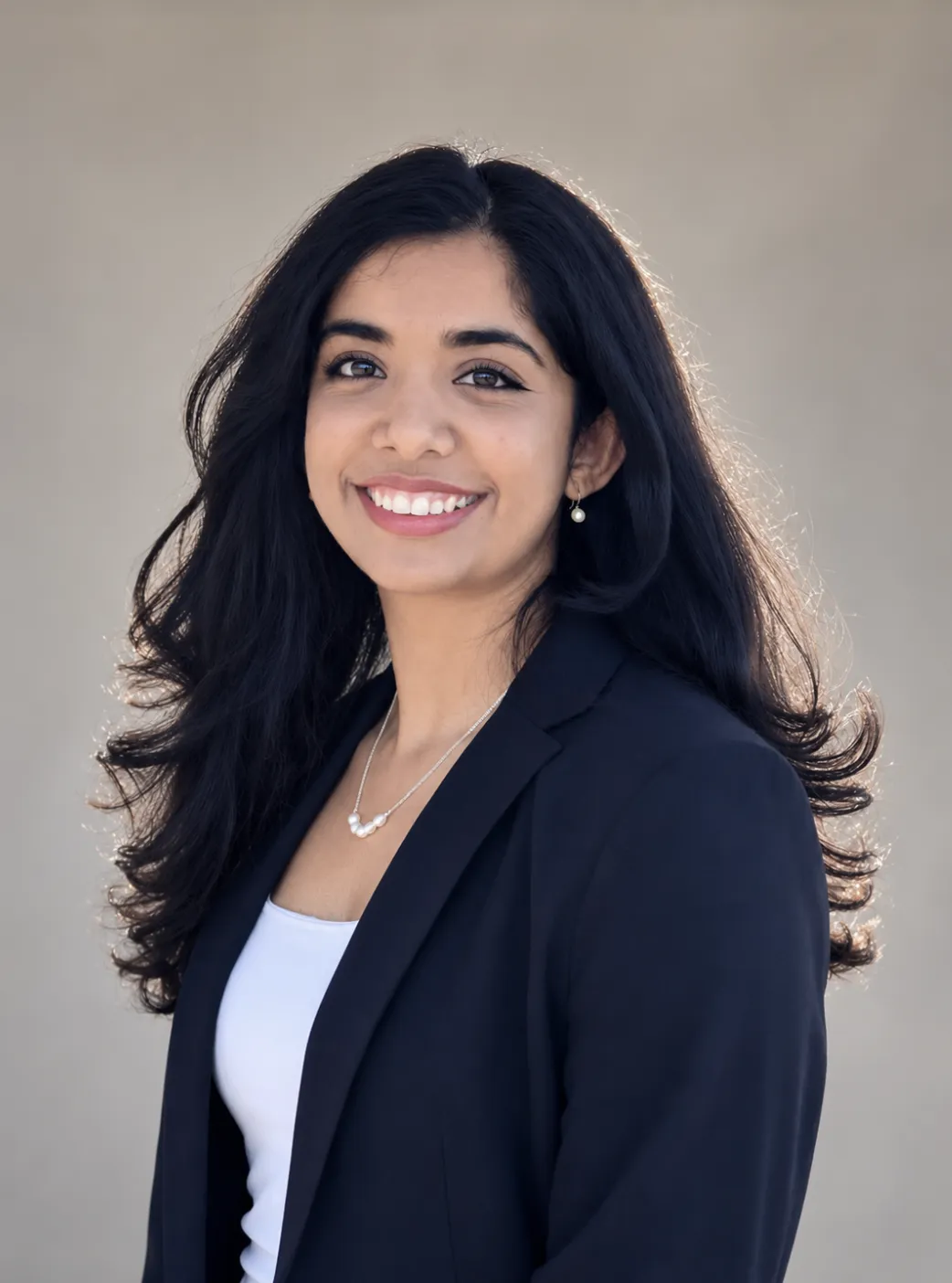 Professional portrait of a smiling woman with long black hair, wearing a black blazer and white top.